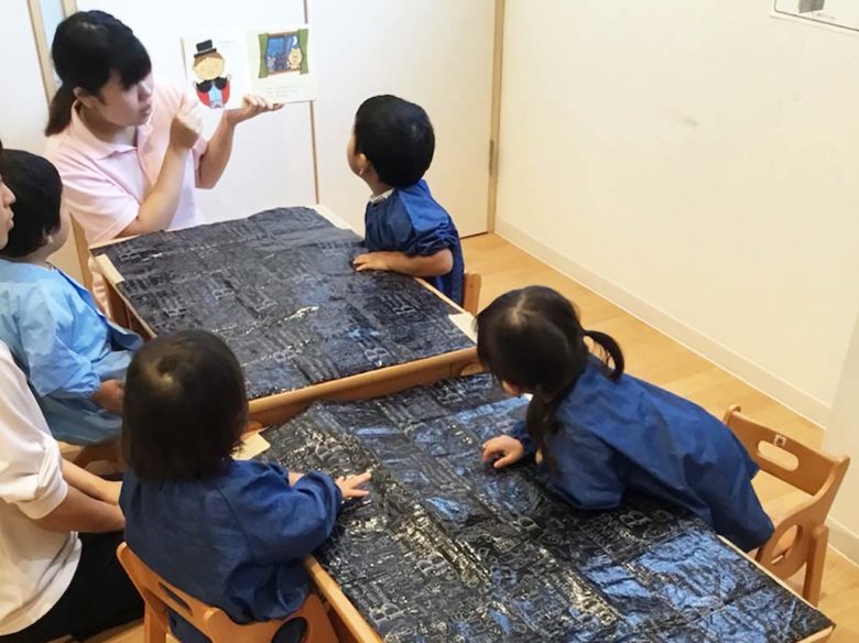 絵本の読み聞かせをする先生と、聞いている子供たち